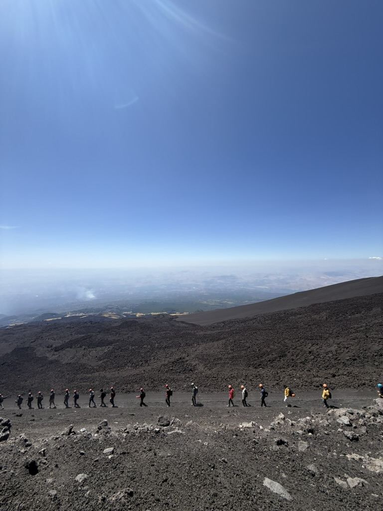Hikers walking the lava trail on Mount Etna with Sicilian plains below